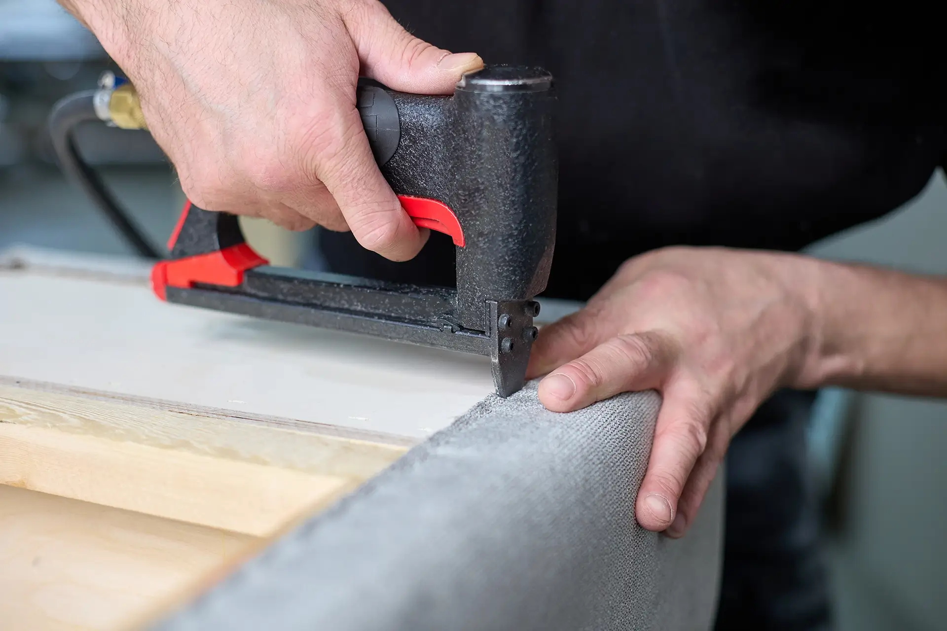 Man with a staple gun fixing the upholstery on a damaged bed.