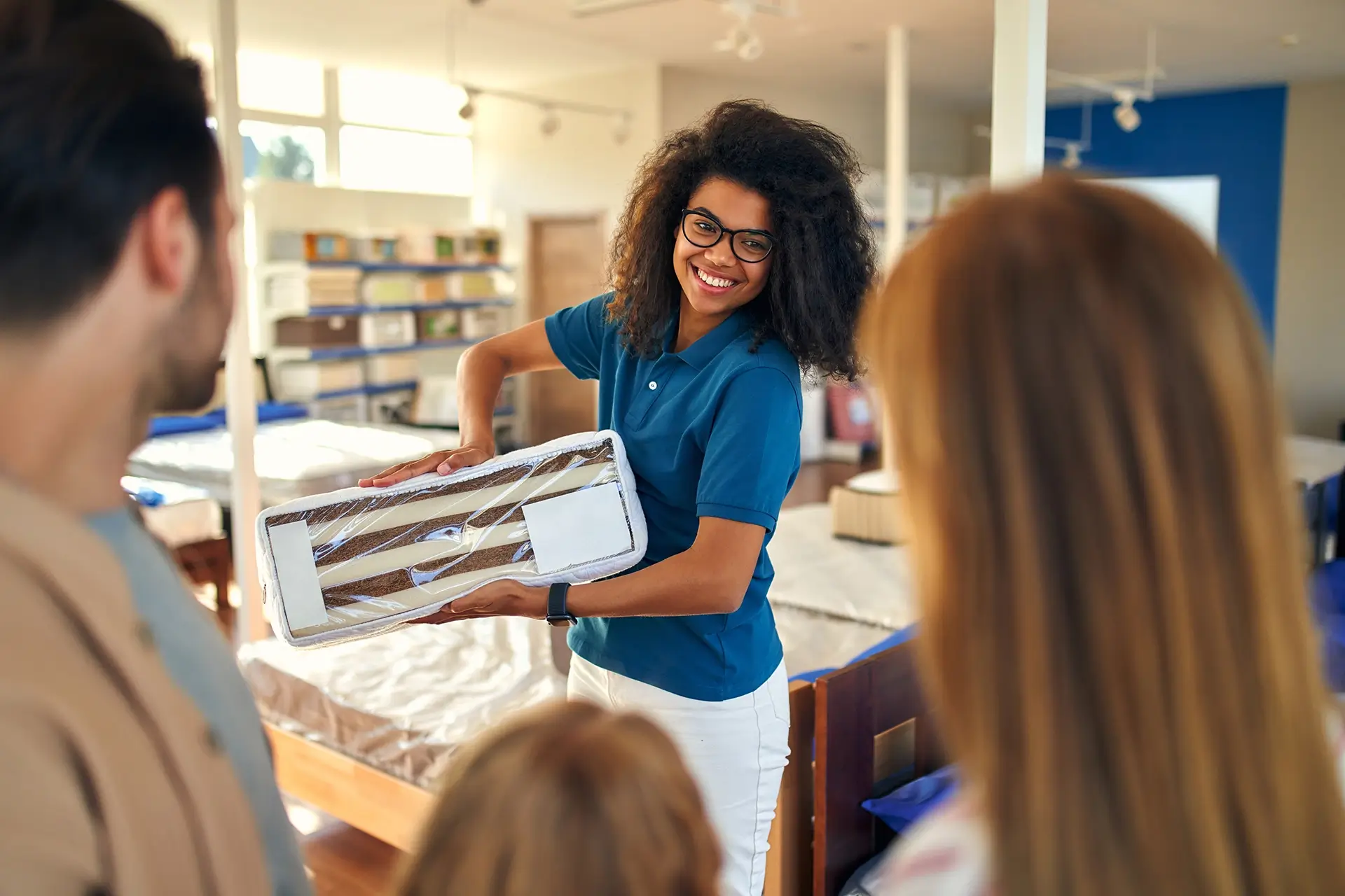 A woman wearing glasses and a blue shirt shows a family the different layers of a mattress in a store.