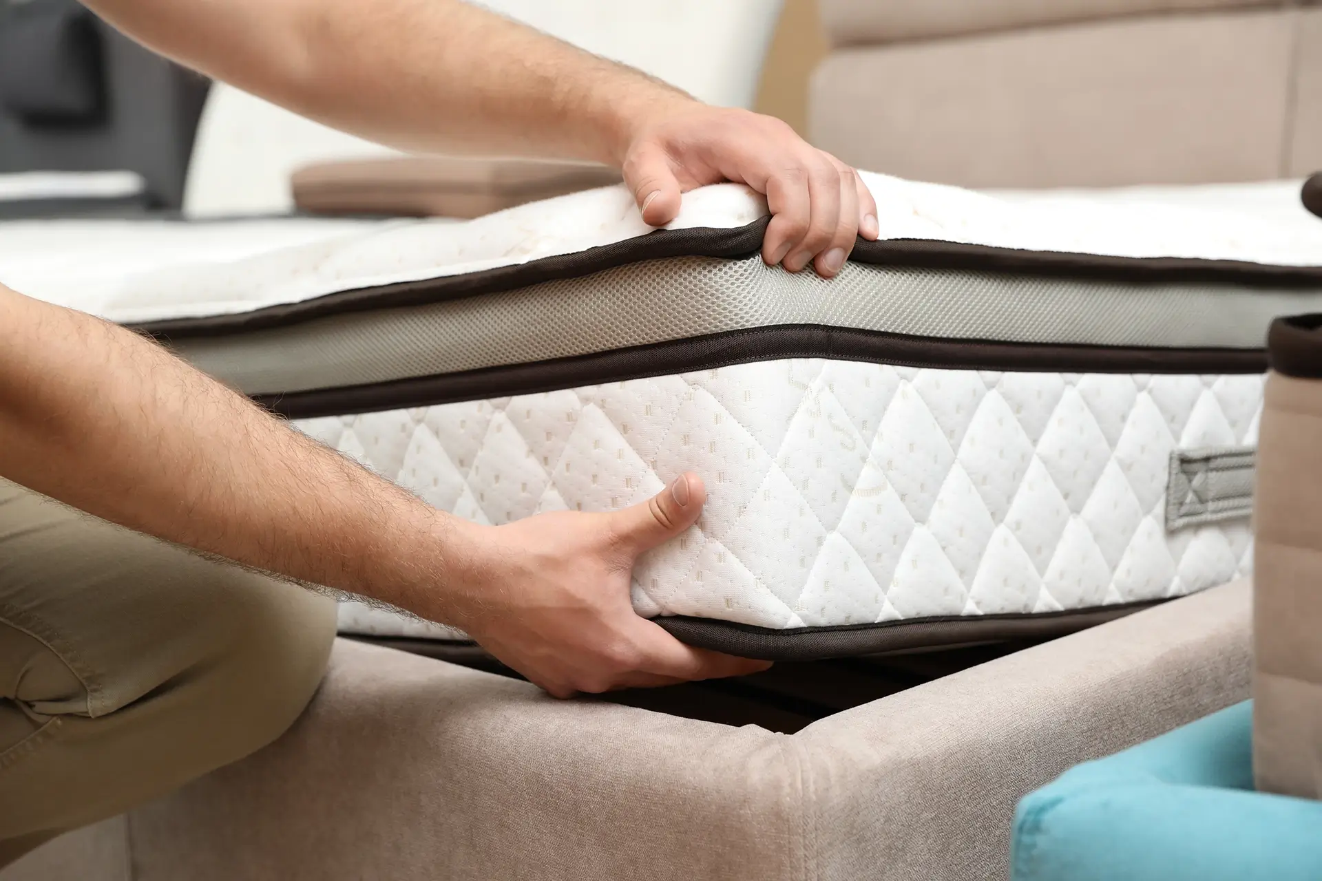 A person lifting a mattress off of a bed frame to inspect the layers and fabrics.