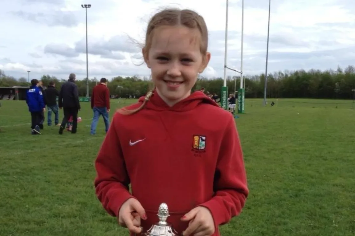 Young Anna in a red hoodie holding a silver trophy.